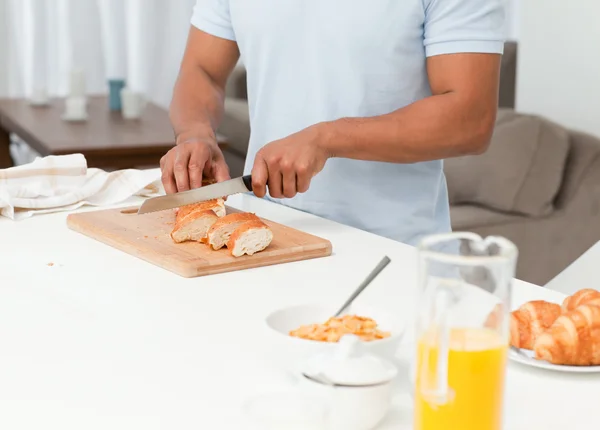 Close up of a man cutting bread during breakfast in his kitchen — Stock Photo, Image