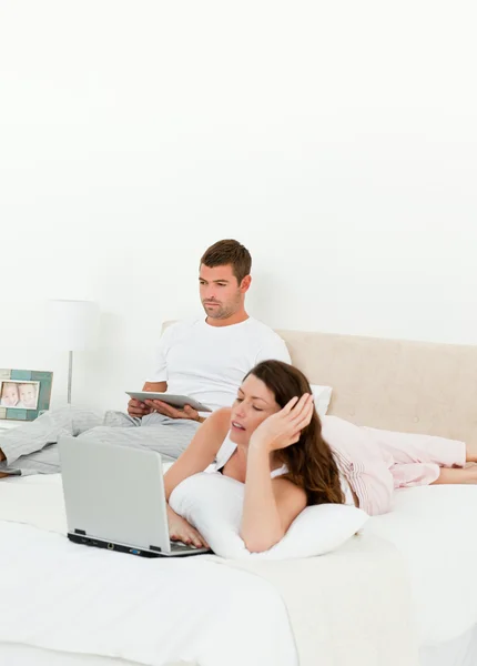 Pretty woman working on her laptop while her husband is reading — Stock Photo, Image