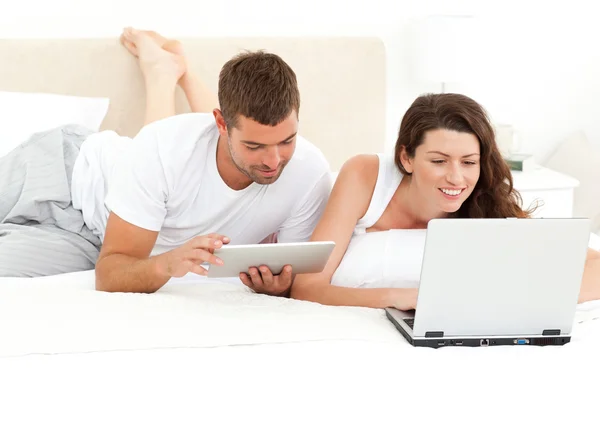 Leuk paar samen te werken op hun laptop liggend op hun bed — Stockfoto