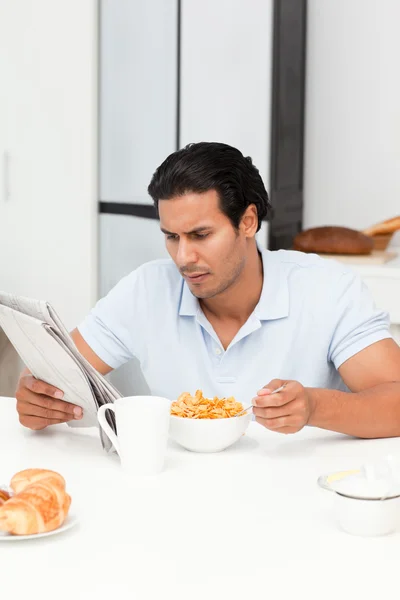 Серьезный человек, читающий газету во время еды зерновых — стоковое фото