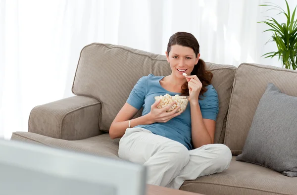 Mulher atraente assistindo televisão e comer milho pop no — Fotografia de Stock