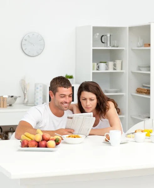 Casal feliz lendo o jornal na cozinha — Fotografia de Stock