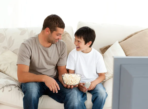 Father and son watching television while eating pop corn on the — Stock Photo, Image