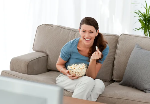 Joyeux femme manger du maïs pop tout en regardant un film à la télévision — Photo