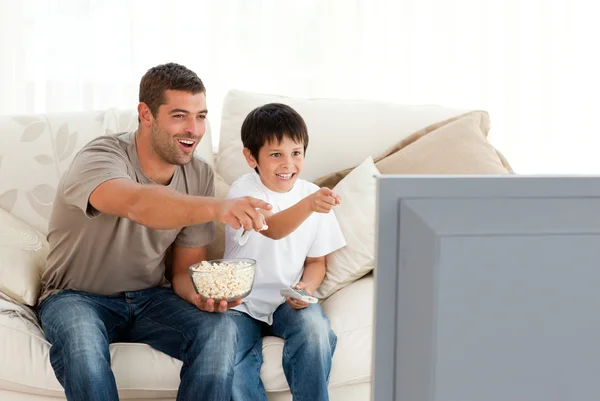 Happy father and son watching television while eating pop corn — Stock Photo, Image