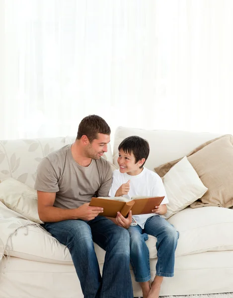 Adorable boy looking at a photo album with his father on the sof — Stock Photo, Image