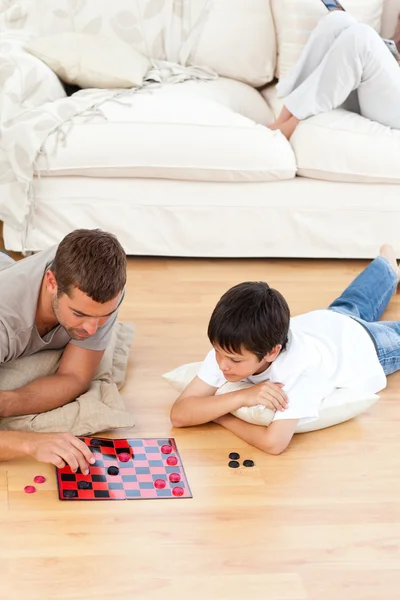 Батько і син грають в шашки разом лежачи на підлозі — стокове фото
