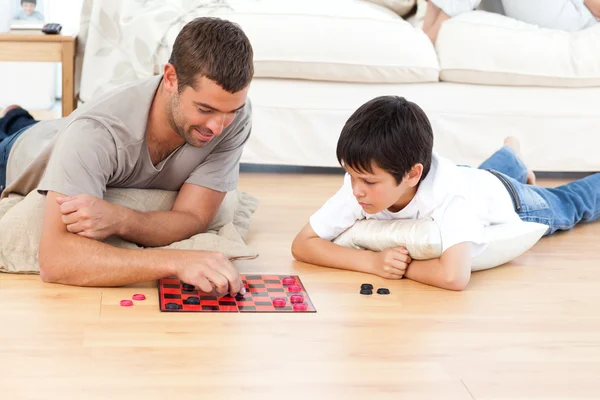 Красивый мужчина играет в шашки со своим сыном, лежащим на полу — стоковое фото