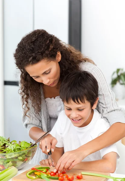 Aufmerksame Mutter hilft ihrem Sohn beim Gemüseschneiden — Stockfoto