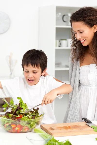 Rapaz bonito misturando uma salada com sua mãe na cozinha — Fotografia de Stock