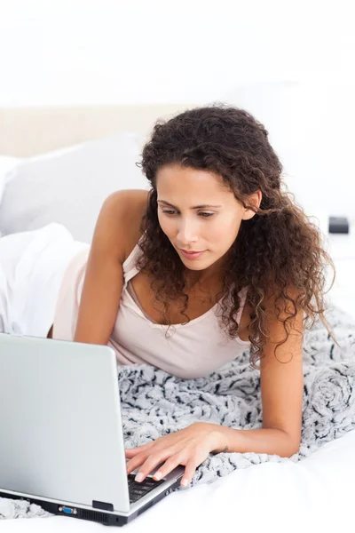 Mulher bonita trabalhando em seu laptop deitado em sua cama — Fotografia de Stock