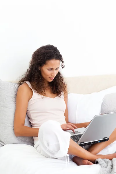 Mujer atractiva trabajando en su computadora portátil sentada en su cama —  Fotos de Stock