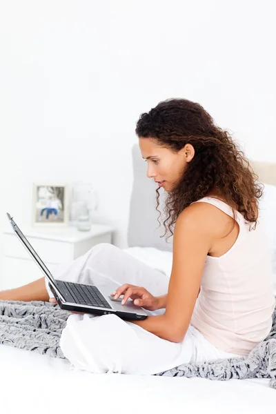 Ciddi İspanyol kadın yatağında oturup onu laptop üzerinde çalışıyor — Stok fotoğraf