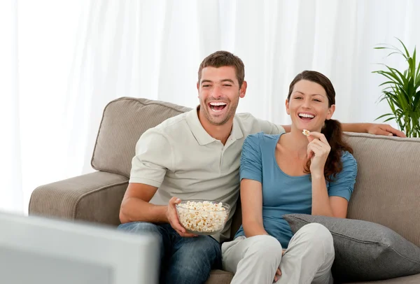 Lovely couple laughing while relaxing in front of the television — Stock Photo, Image
