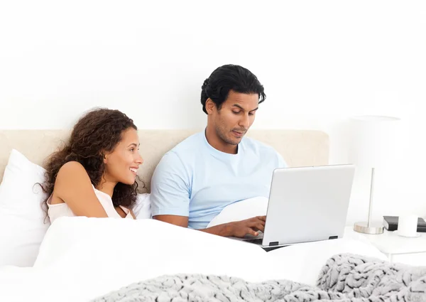 Happy woman looking her husband working on his laptop on the bed — Stock Photo, Image