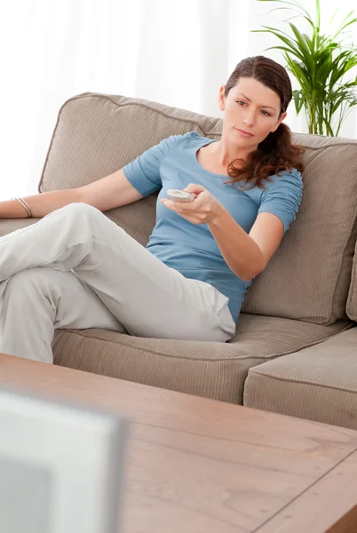 Ernste Frau wechselt den Kanal, während sie sich im Wohnzimmer entspannt — Stockfoto