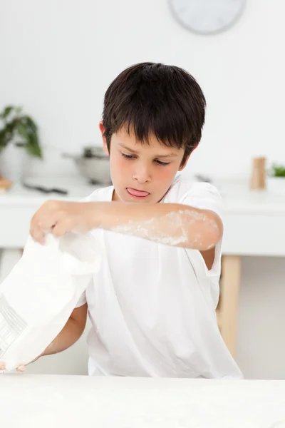 Cute boy pouring flour on a table in his kitchen — Stock Photo, Image