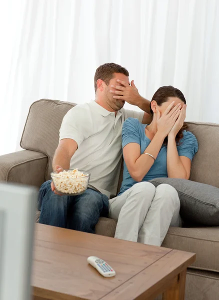 Encantador casal escondendo seu rosto de um filme de terror sentado em t — Fotografia de Stock