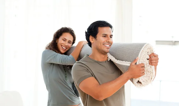 Casal feliz segurando um tapete juntos em sua nova sala de estar — Fotografia de Stock