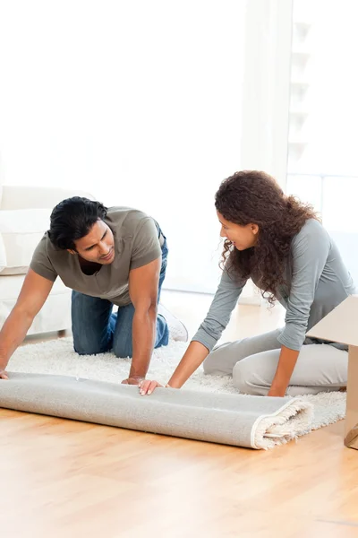 Preciosa pareja enrollando una alfombra juntos en la sala de estar —  Fotos de Stock