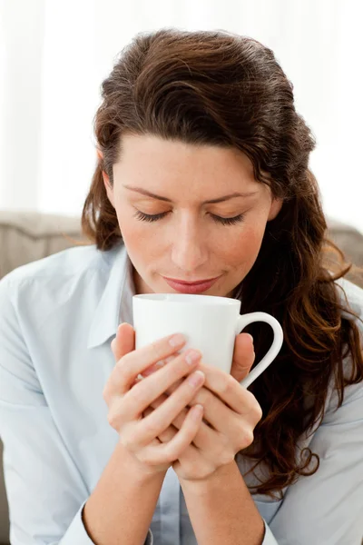 Mulher de negócios bonita cheirando seu café sentado no sofá — Fotografia de Stock