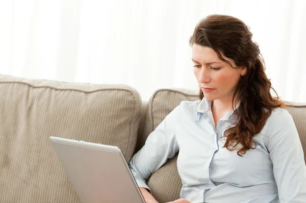Mulher de negócios séria trabalhando em seu laptop no sofá — Fotografia de Stock