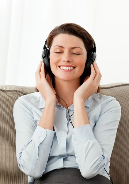 Leende kvinna lyssnar musik med hörlurarna i vardagsrummet — Stockfoto