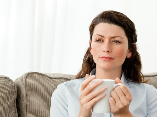 Задумчивая женщина пьет кофе на диване — стоковое фото