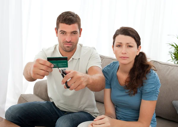 Pareja preocupada cortando su tarjeta de crédito juntos sentados en el — Foto de Stock