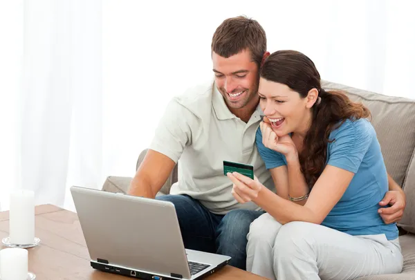Счастливая пара смотрит на свои счета онлайн сидя на софе — стоковое фото