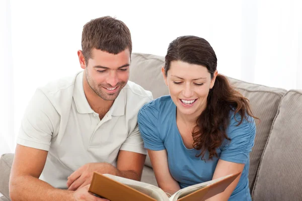 Adorável casal lendo um livro juntos no sofá — Fotografia de Stock