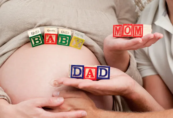 Primer plano de los futuros padres sosteniendo cubos formando las palabras mamá, papá y bebé — Foto de Stock