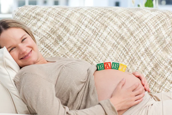 Hübsche zukünftige Mutter mit Babybuchstaben auf dem Bauch — Stockfoto