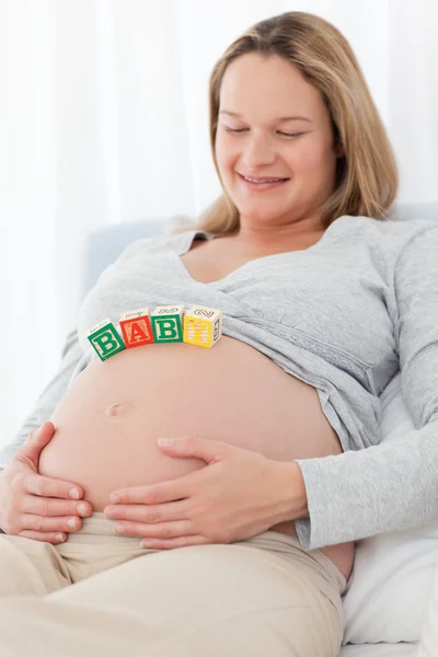 Linda mujer embarazada con letras de mamá en su vientre relajante — Foto de Stock