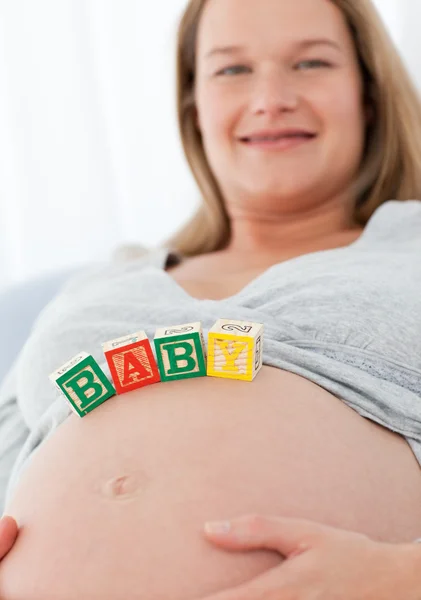 Vrolijke zwangere vrouw met baby letters op haar buik — Stockfoto