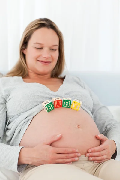 Mulher grávida alegre com letras de bebê em sua barriga — Fotografia de Stock