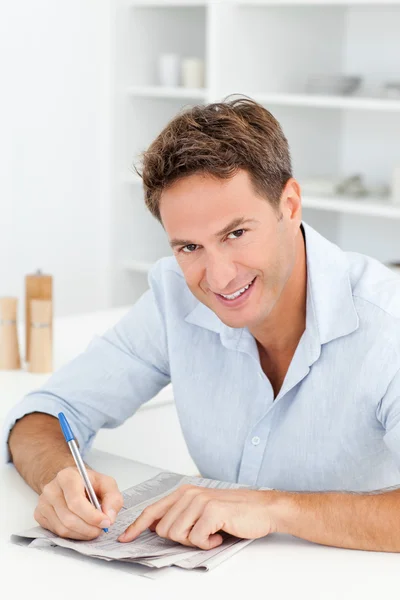 Smart man doing a cryptic crossword sitting in his kitchen — Stock Photo, Image