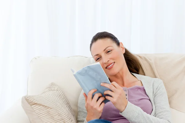 Mujer encantadora leyendo un romance sentado en el sofá —  Fotos de Stock