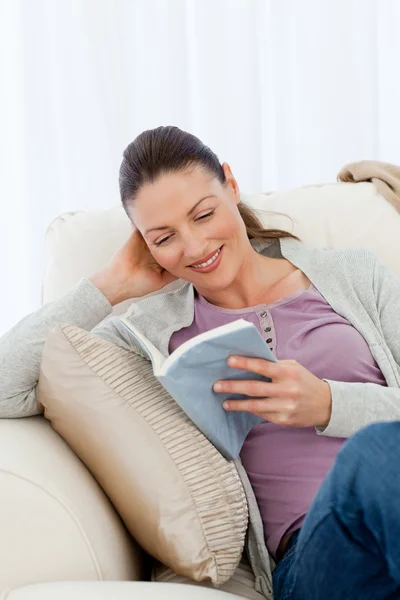 Mulher bonito ler um romance sentado no sofá — Fotografia de Stock