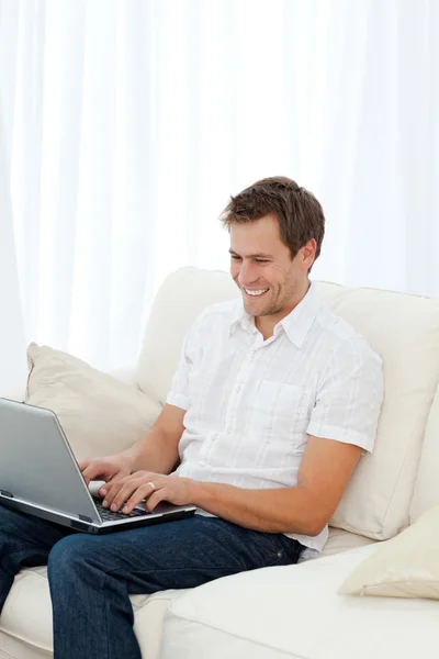 Człowiek śmiechu podczas pracy na swoim laptopie na kanapie — Zdjęcie stockowe
