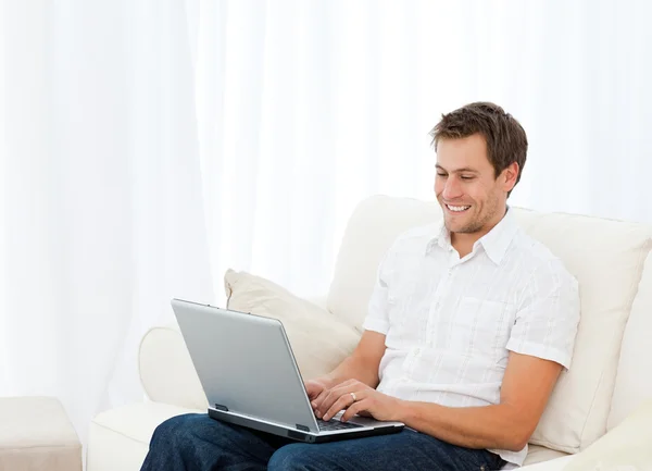 Bonito homem trabalhando em seu laptop enquanto relaxa no sofá — Fotografia de Stock