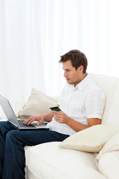Позитивный человек покупает онлайн сидя на диване — стоковое фото