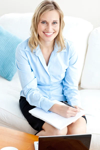 Radiant businesswoman writing in her notepad and using her lapto Stock Image