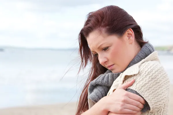 浜辺のセーターを着ていると寒くなって不幸な女性 ストック写真