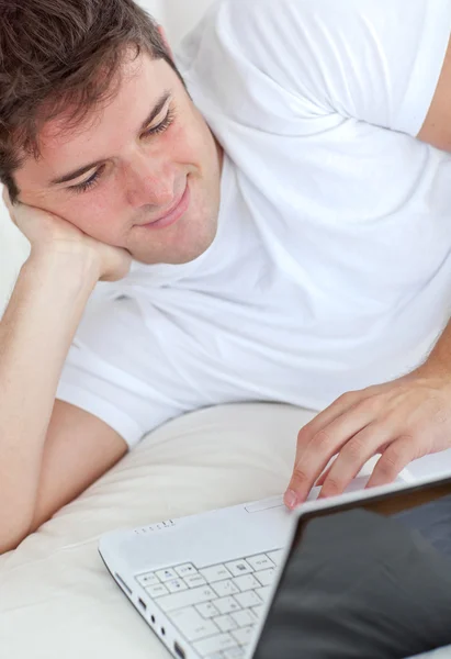 Gülümseyen adam onun yatakta yatarken onun laptop kullanma — Stok fotoğraf