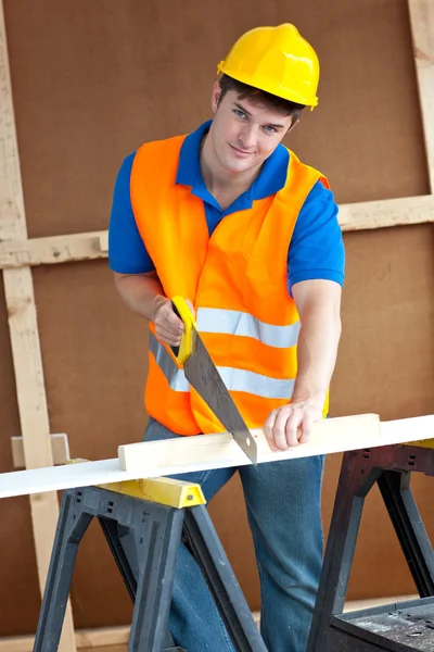 Charismatic male worker wearing a yellow hardhat sawing a wooden Stock Photo