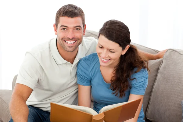 Pretty woman reading a book with her boyfriend on the sofa — Stock Photo, Image