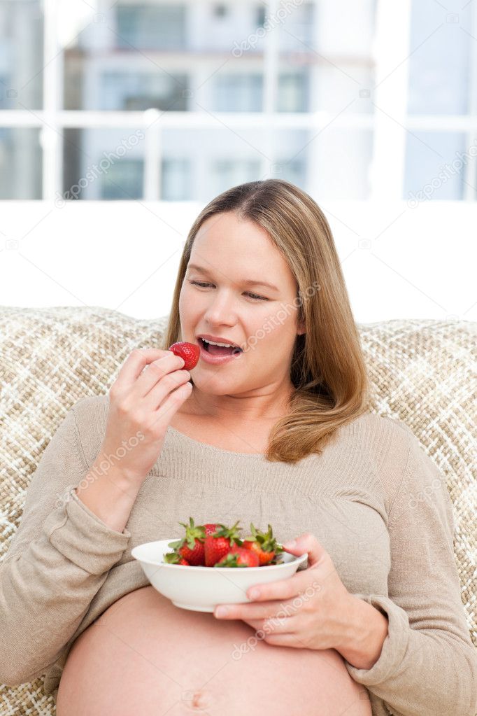 Hungry pregnant woman eating strawberries sitting in the living ...