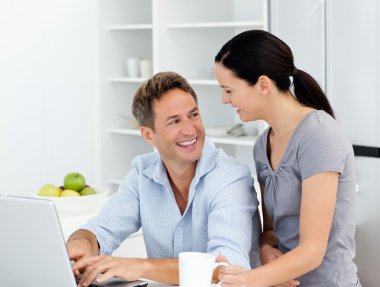 Happy couple working on their laptop in the kitchen clipart