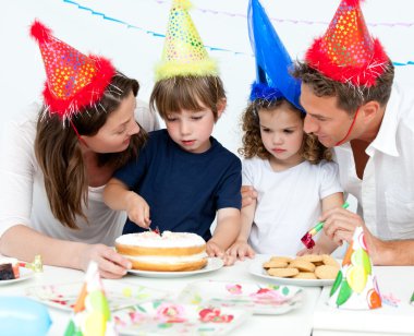 Cute little boy cutting a birthday cake for his family clipart